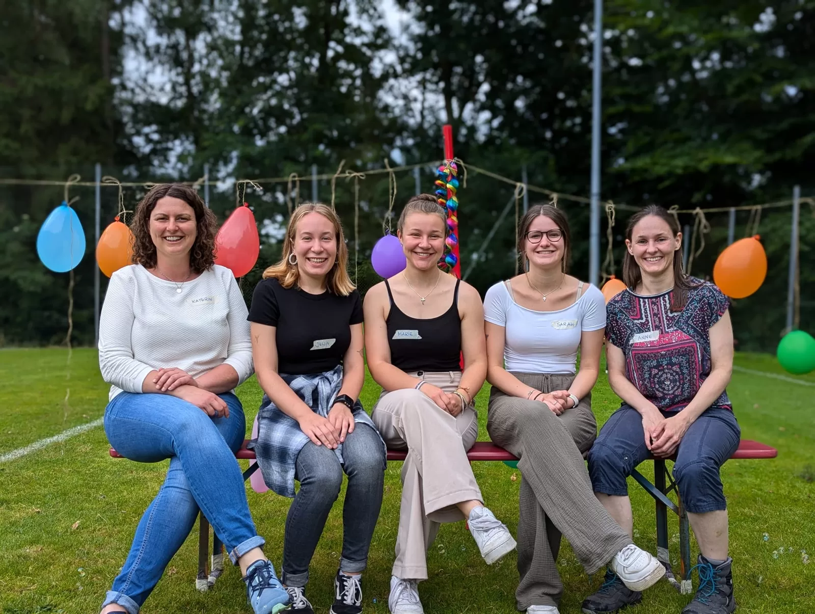 fünf Frauen auf einer Bank sitzend, lachend mit Luftballons im Hintergrund